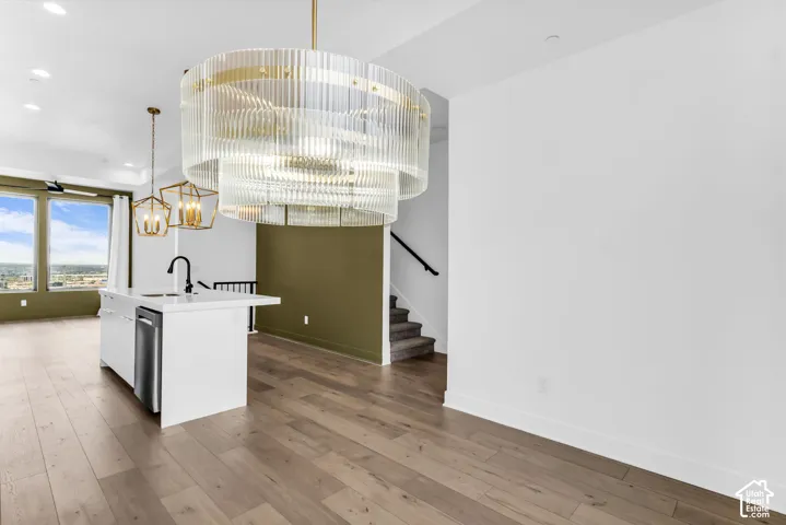 Open-concept living space with wide-plank wood-finish flooring, a contemporary kitchen island with a built-in sink, and a multi-tiered chandelier