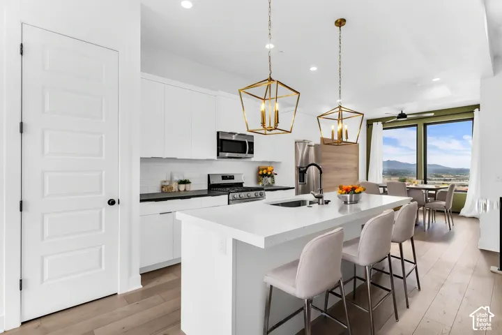 AI Staged - Modern kitchen featuring a large island with sink, stainless steel appliances, white cabinetry, and wood-finish flooring