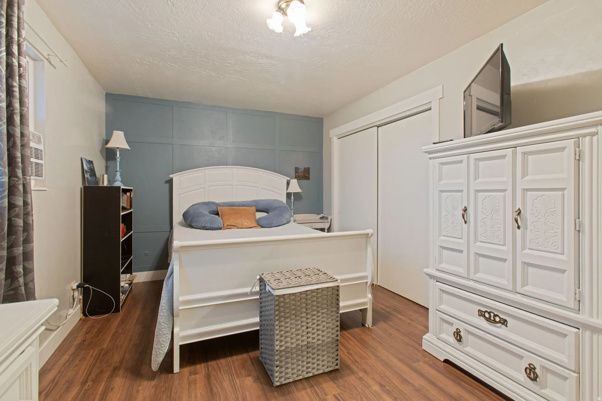 Wood-finish flooring, accent wall with paneling, window with trim, and a built-in closet with sliding doors
