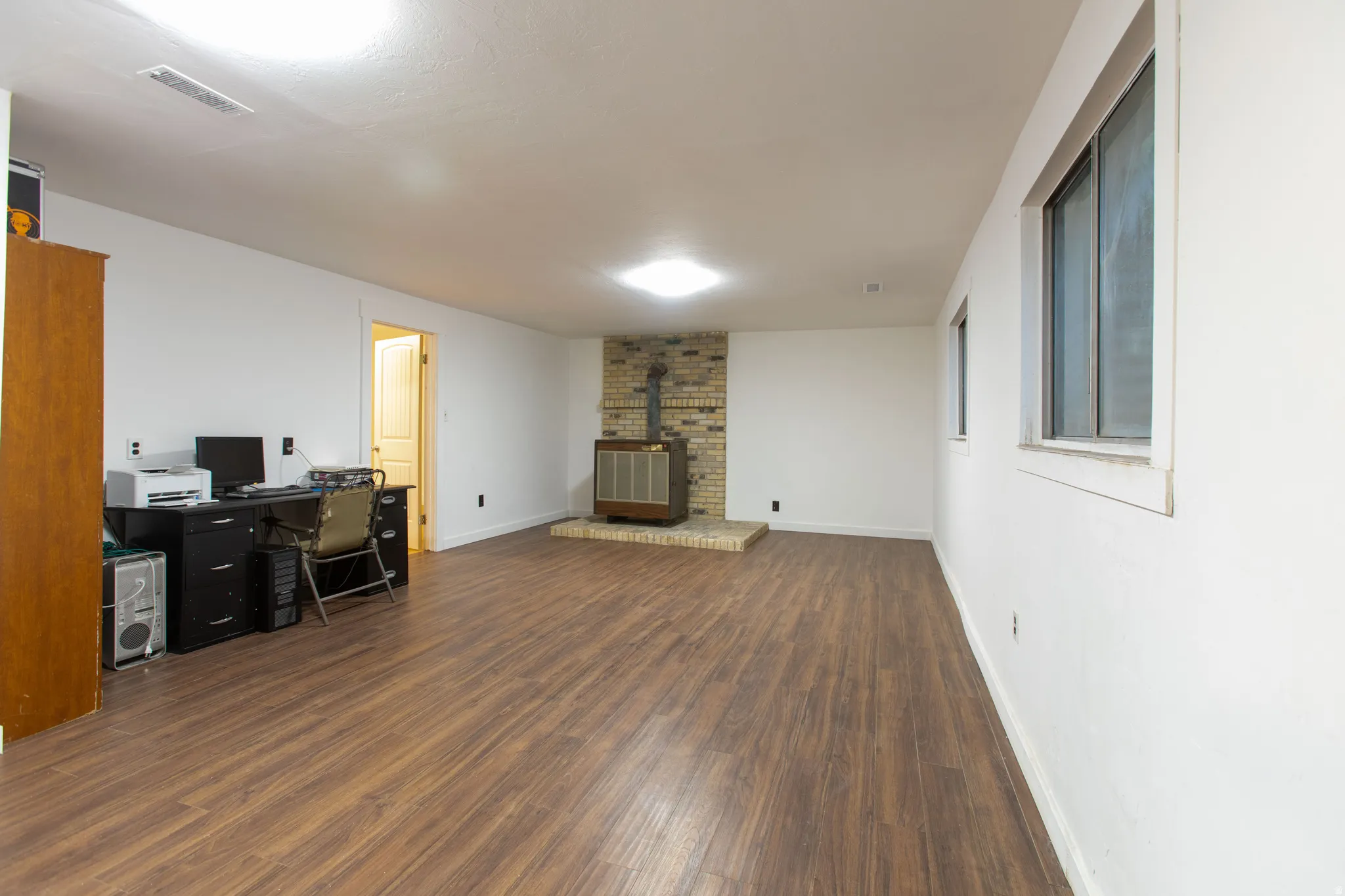 Spacious room with wood-finish flooring, a brick-surround wood-burning stove, and multiple windows