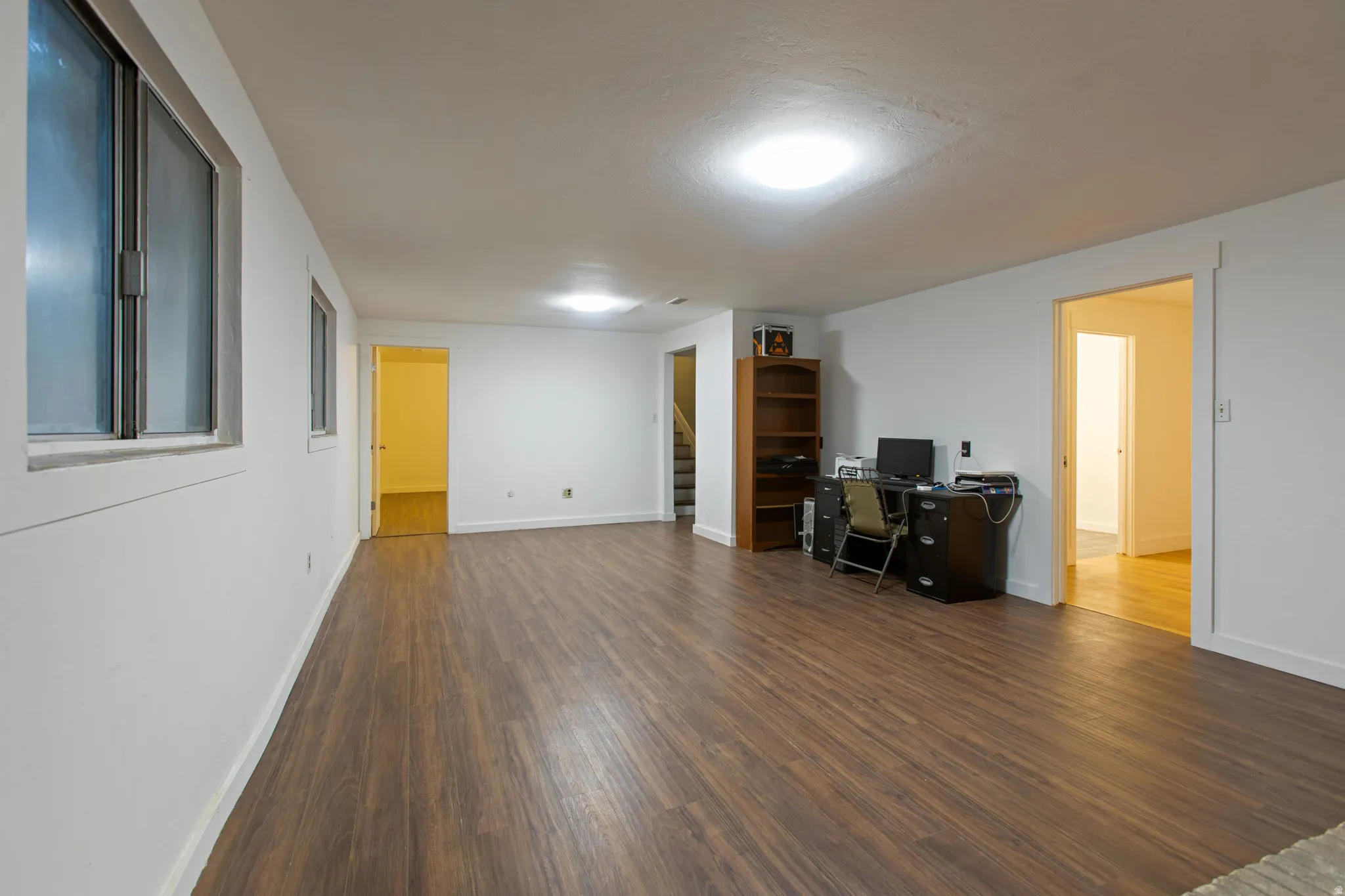 Spacious room featuring wood-finish flooring, white walls, multiple windows, and recessed lighting