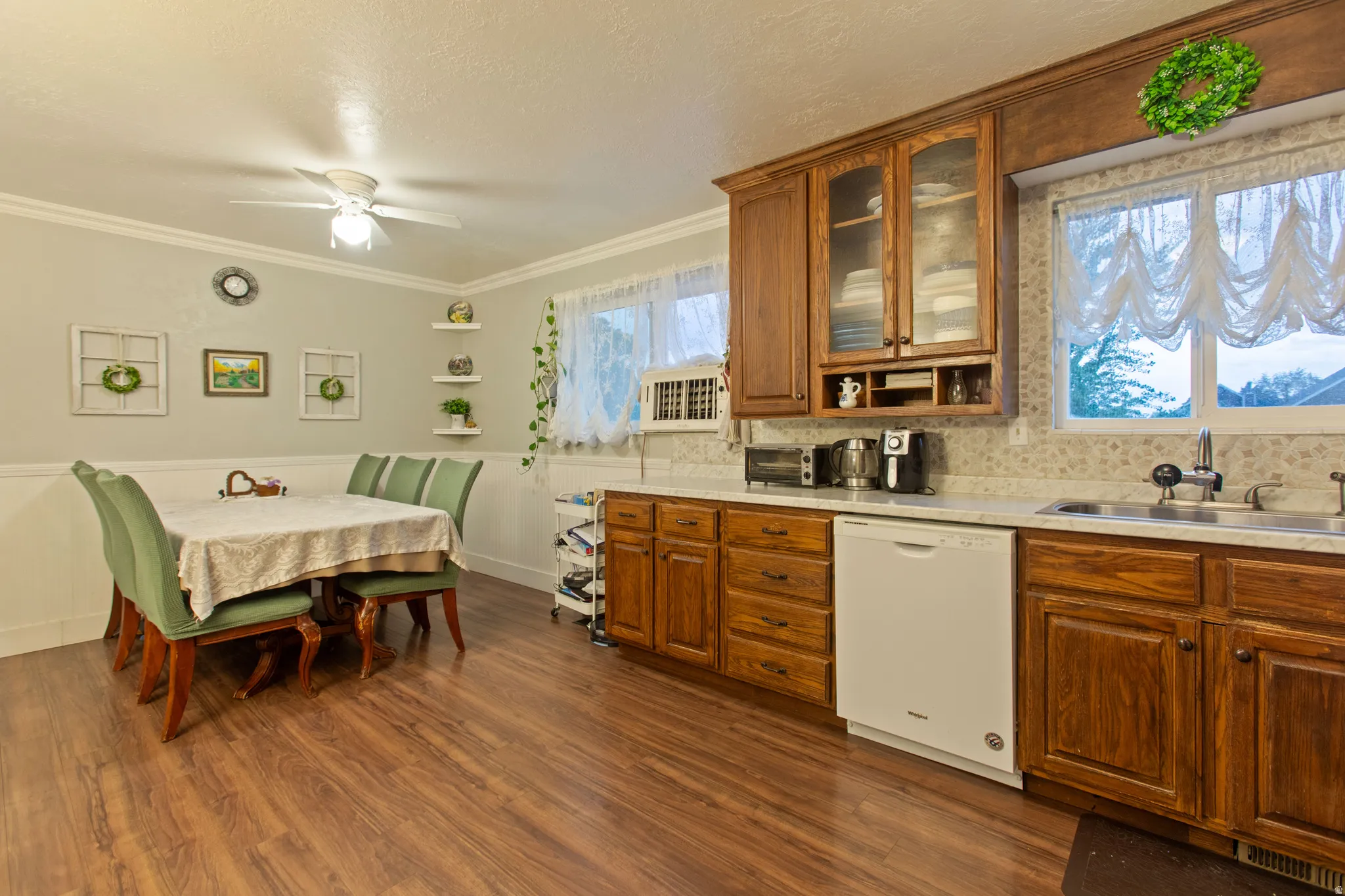 Wood-finish flooring, white paneled wainscoting, ceiling fan with integrated lighting, wood cabinetry, and a double basin sink