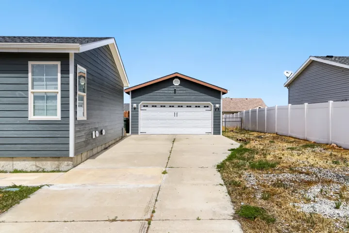 Detached garage with white overhead door, concrete driveway, and durable siding on both structures