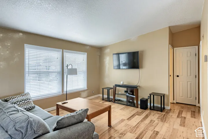 Wood-finish flooring throughout, multiple windows with blinds, neutral wall tones, and a paneled door