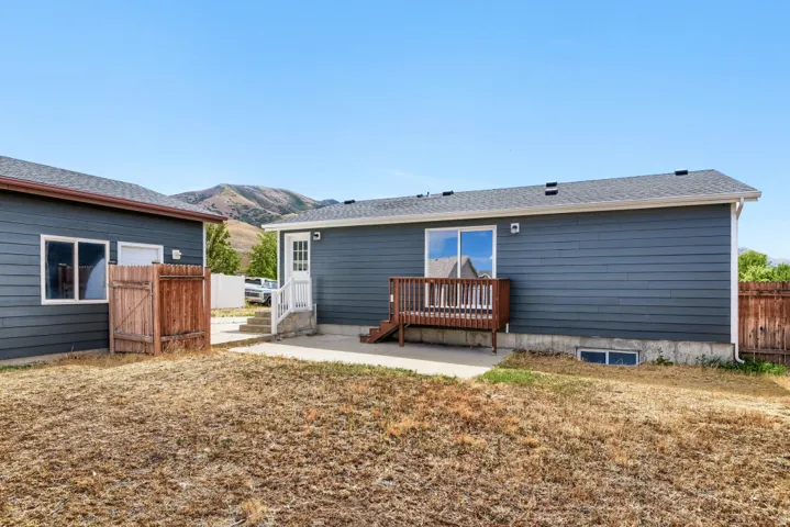Exterior featuring dark blue siding, a wooden deck, sliding glass door, white trim windows, and a concrete patio