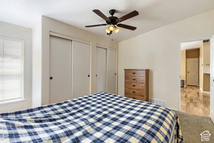 Spacious bedroom featuring triple sliding-door closets with mirrored panels, wood-finish dresser with multiple drawers, ceiling fan with integrated lighting, carpet flooring, and access to adjacent bathroom and hallway spaces