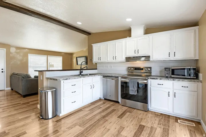 Kitchen featuring white cabinetry, wood-finish flooring, stainless steel appliances, and a pass-through counter