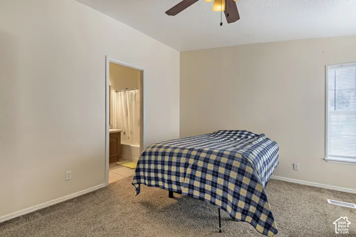 Carpeted room with a ceiling fan, window with blinds, and an attached bathroom featuring a built-in vanity and bathtub