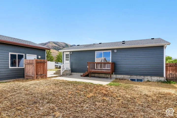 Exterior featuring dark blue siding, a wooden deck, sliding glass door, white trim windows, and a concrete patio