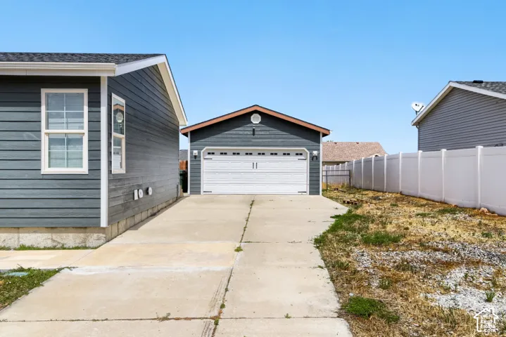Detached garage with white overhead door, concrete driveway, and durable siding on both structures