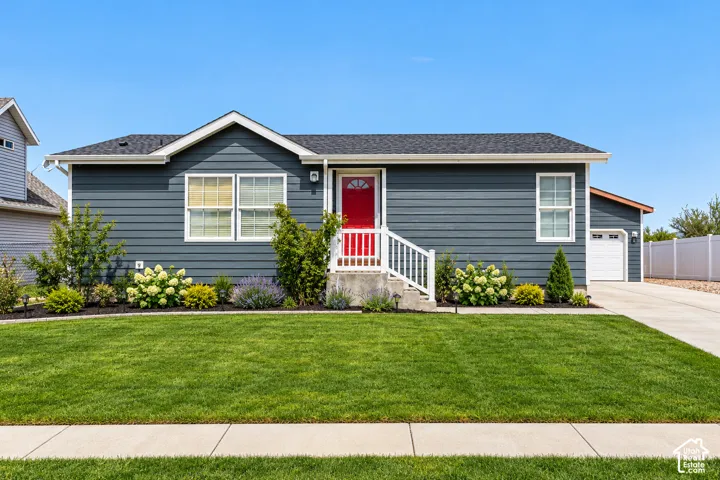 Single-story residence featuring horizontal lap siding, a pitched asphalt shingle roof, a red front door with an arched glass inset, a white handrail entry, and an attached garage
