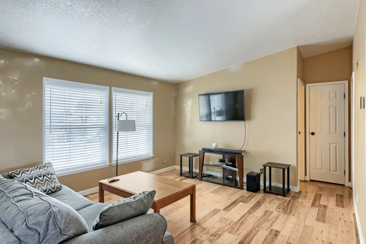 Wood-finish flooring throughout, multiple windows with blinds, neutral wall tones, and a paneled door