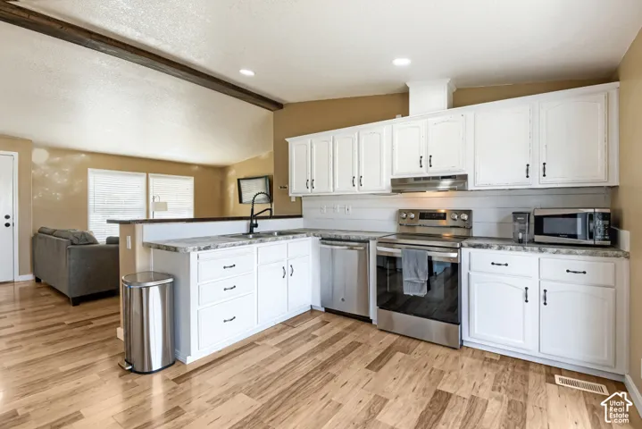 Kitchen featuring white cabinetry, wood-finish flooring, stainless steel appliances, and a pass-through counter