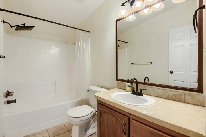 White rectangular shower/tub with a rain showerhead, single-sink vanity with a light-colored countertop, and wood-finish cabinetry