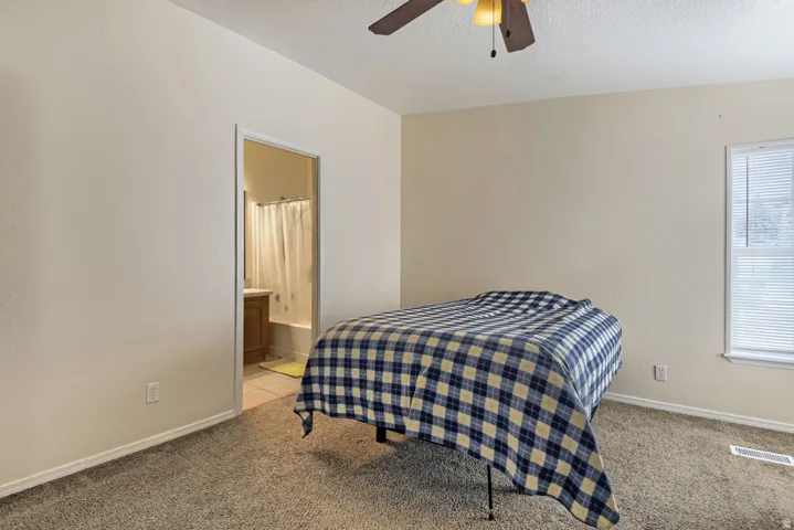 Carpeted room with a ceiling fan, window with blinds, and an attached bathroom featuring a built-in vanity and bathtub