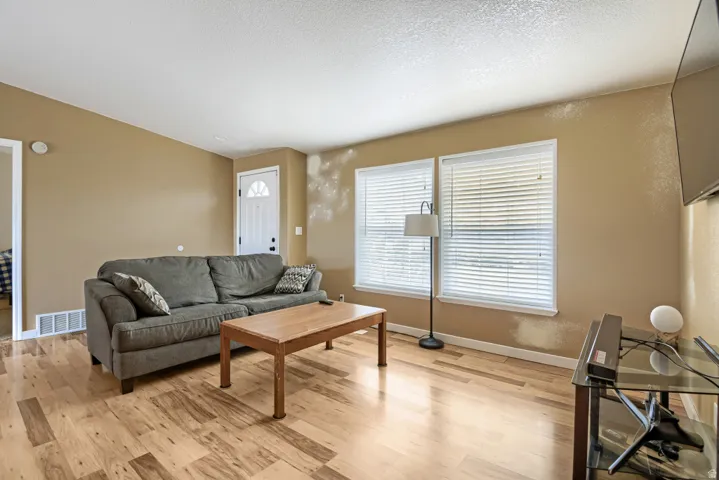 Wood-finish flooring, multiple windows with blinds, and a paneled entry door with frosted glass insert