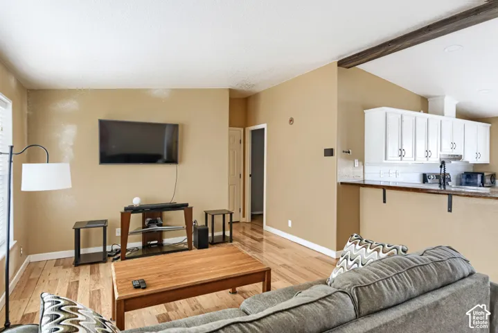 Wood-finish flooring throughout, vaulted ceiling with exposed beam, white cabinetry with dark hardware, built-in range hood, and a breakfast bar