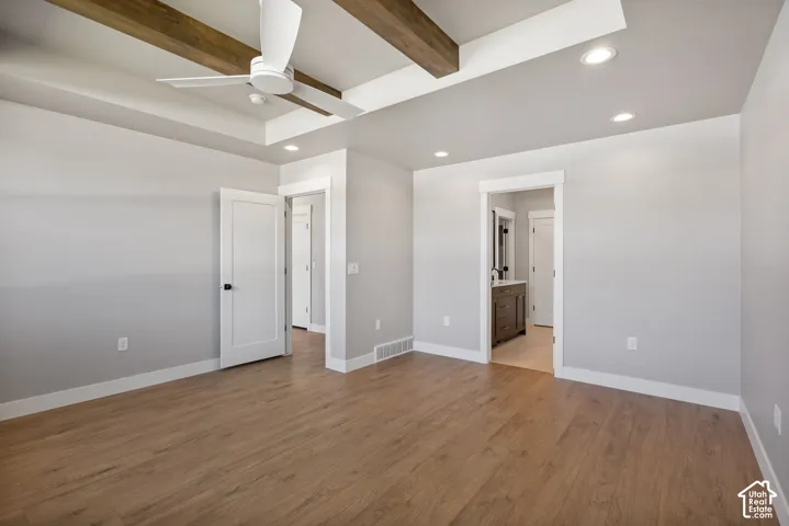 Tray ceiling with exposed wood beams, wood-finish flooring, recessed lighting, white interior doors with black hardware, and an en suite with a dark wood vanity