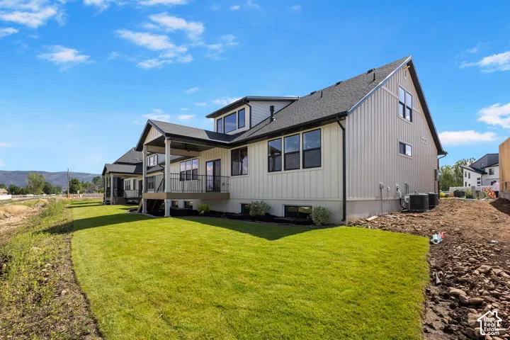 Expansive backyard featuring a manicured lawn, a covered porch with black railings, and multiple large windows