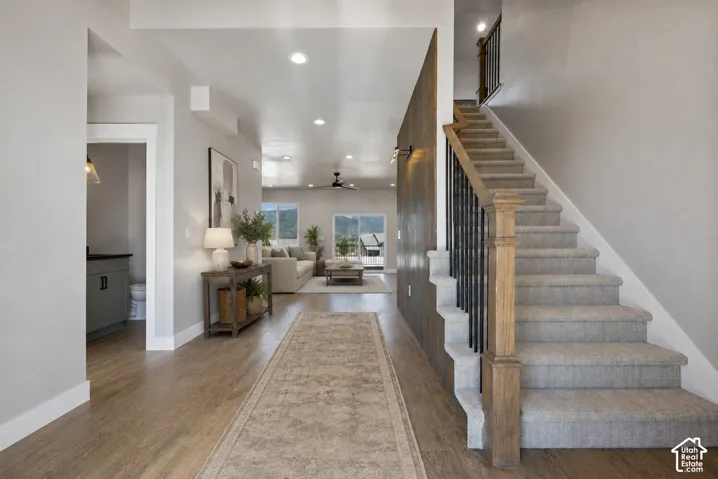 Spacious entry with wood-finish flooring, staircase featuring carpeted treads and wood newel post with black metal spindles, recessed lighting, and a powder room with a dark-finish vanity