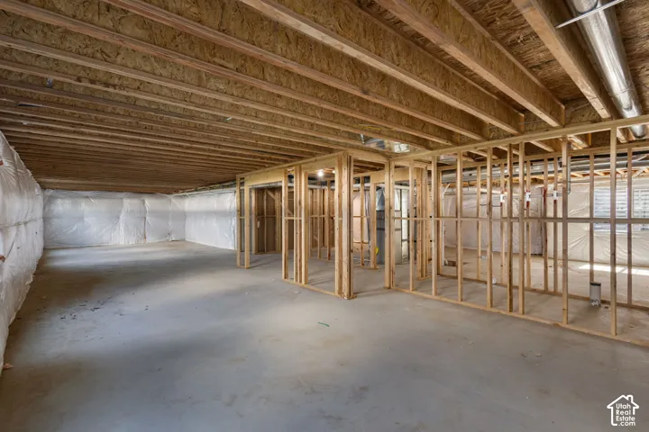 Unfinished basement featuring exposed wood joists, structural framing, concrete flooring, and insulated walls
