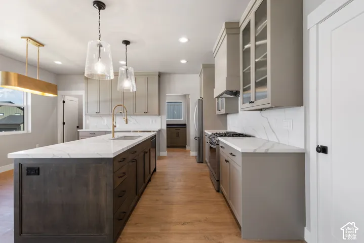 Contemporary kitchen featuring an expansive center island with an integrated sink, light wood-finish flooring, recessed lighting, and modern pendant light fixtures