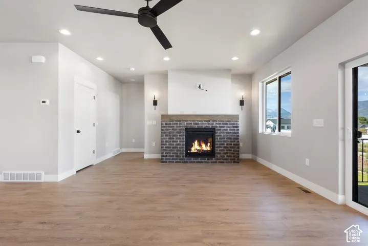 Spacious living area featuring wood-finish flooring, a brick-surround fireplace with a wood mantle, a black ceiling fan, and recessed lighting
