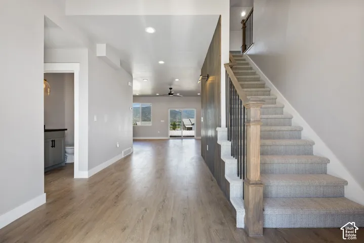 Wood-finish flooring, recessed lighting, carpeted staircase with wood newel posts and metal spindles, and a wall-mounted light fixture