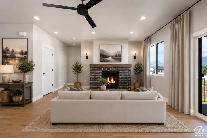 Recessed lighting, wood-finish flooring, black brick-surround fireplace with a wood mantle, ceiling fan, and large windows