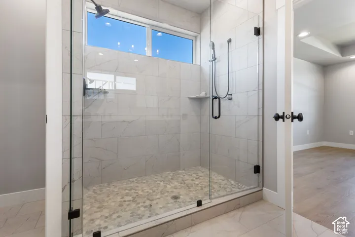 Frameless glass shower enclosure with matte black hardware, tiled walls, pebble shower floor, and an integrated shower niche