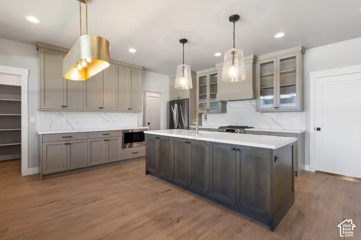Spacious kitchen featuring an expansive center island, modern pendant lighting, wood-finish flooring, a built-in microwave, and a pantry with shelving