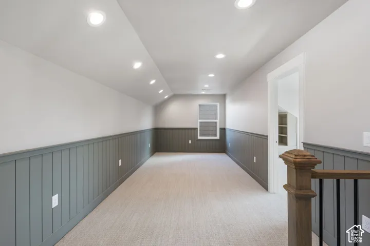 Recessed lighting, sloped ceiling, wainscoting, light-toned carpeting, and wood newel post with metal balusters