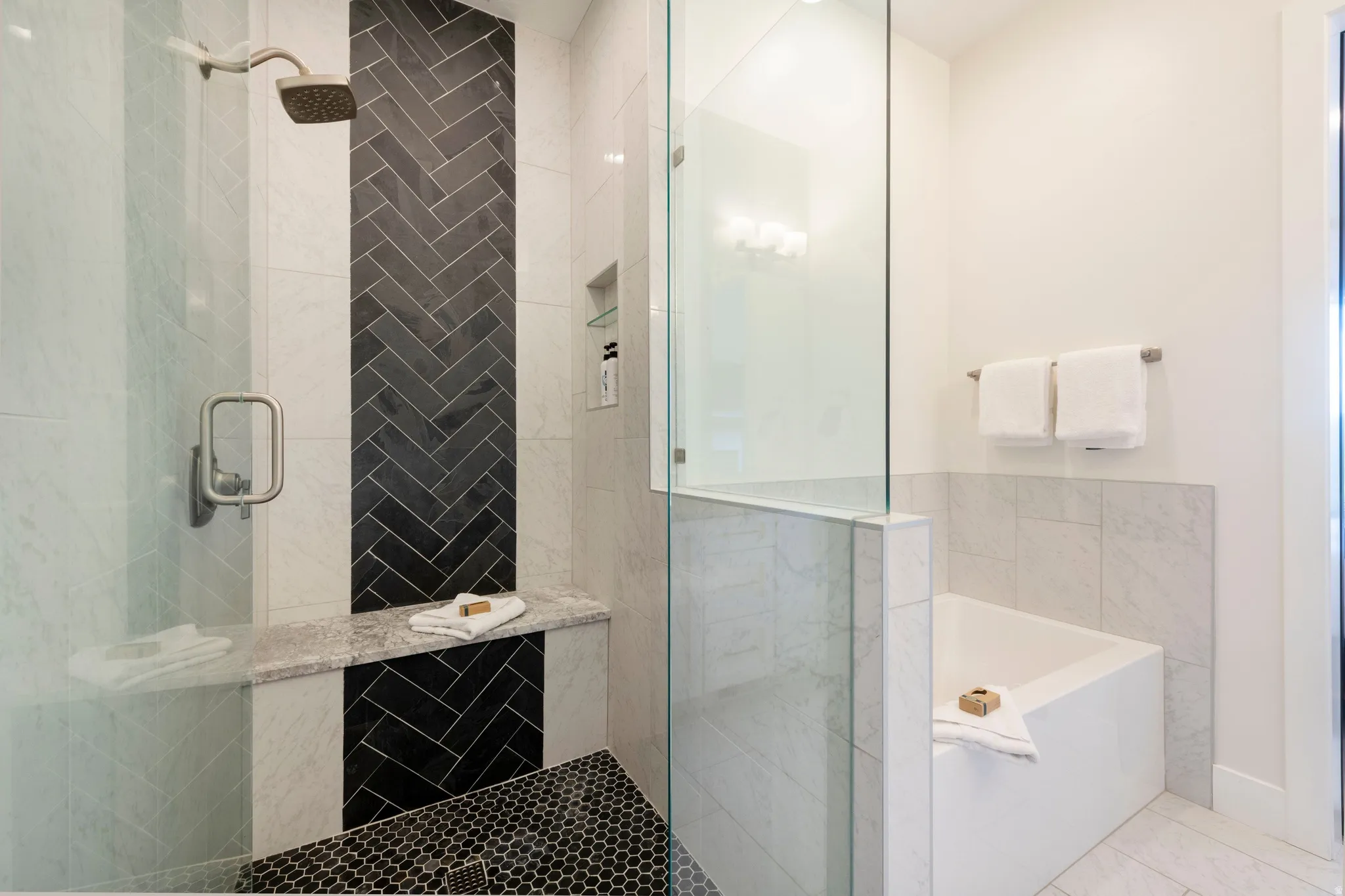 Shower with a rain showerhead, a built-in bench, and black herringbone tile detailing