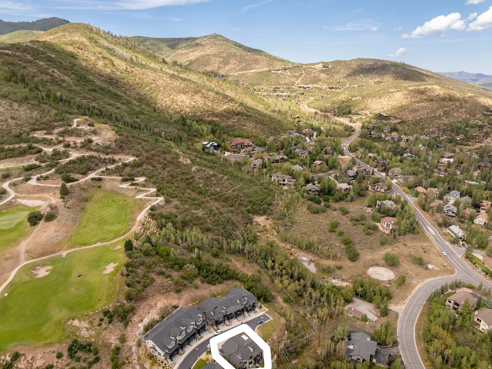 Mountainous terrain with natural vegetation, golf course frontage, paved roadways, and a cluster of townhomes