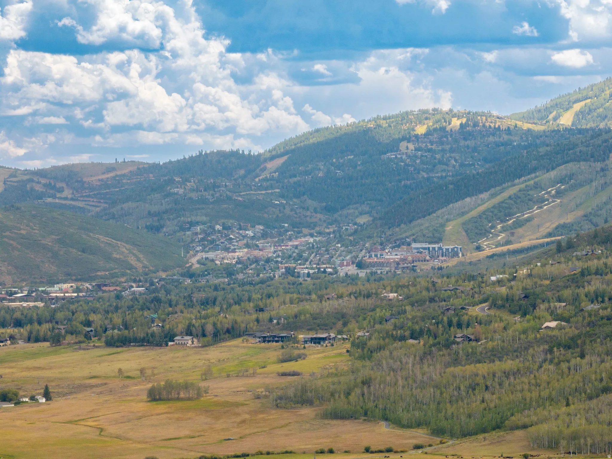Expansive mountain terrain featuring scattered structures, forested slopes, open fields, and distant developed areas