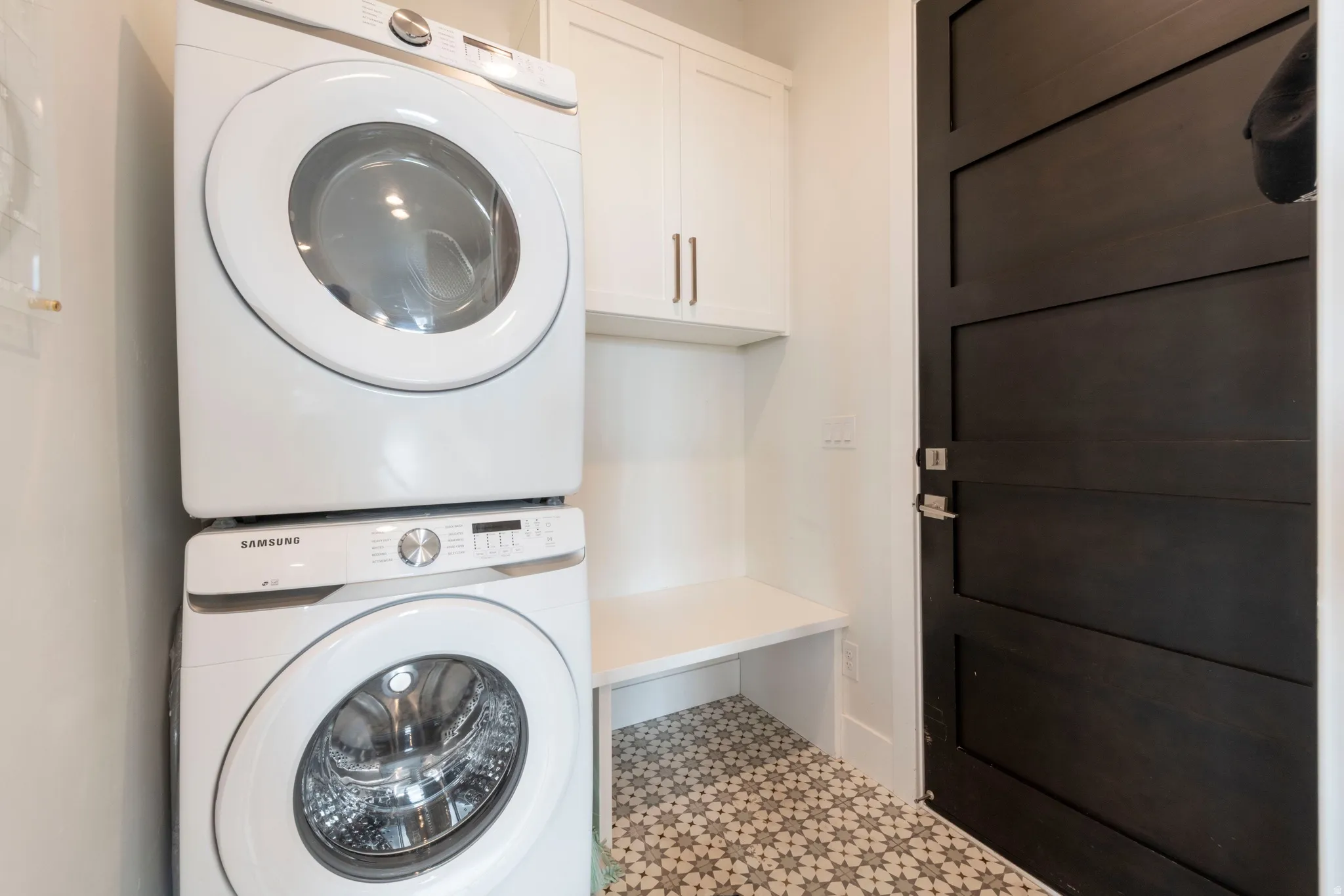 Laundry area featuring a stacked washer and dryer, patterned floor tile, built-in cabinetry, and a dark wood panel door