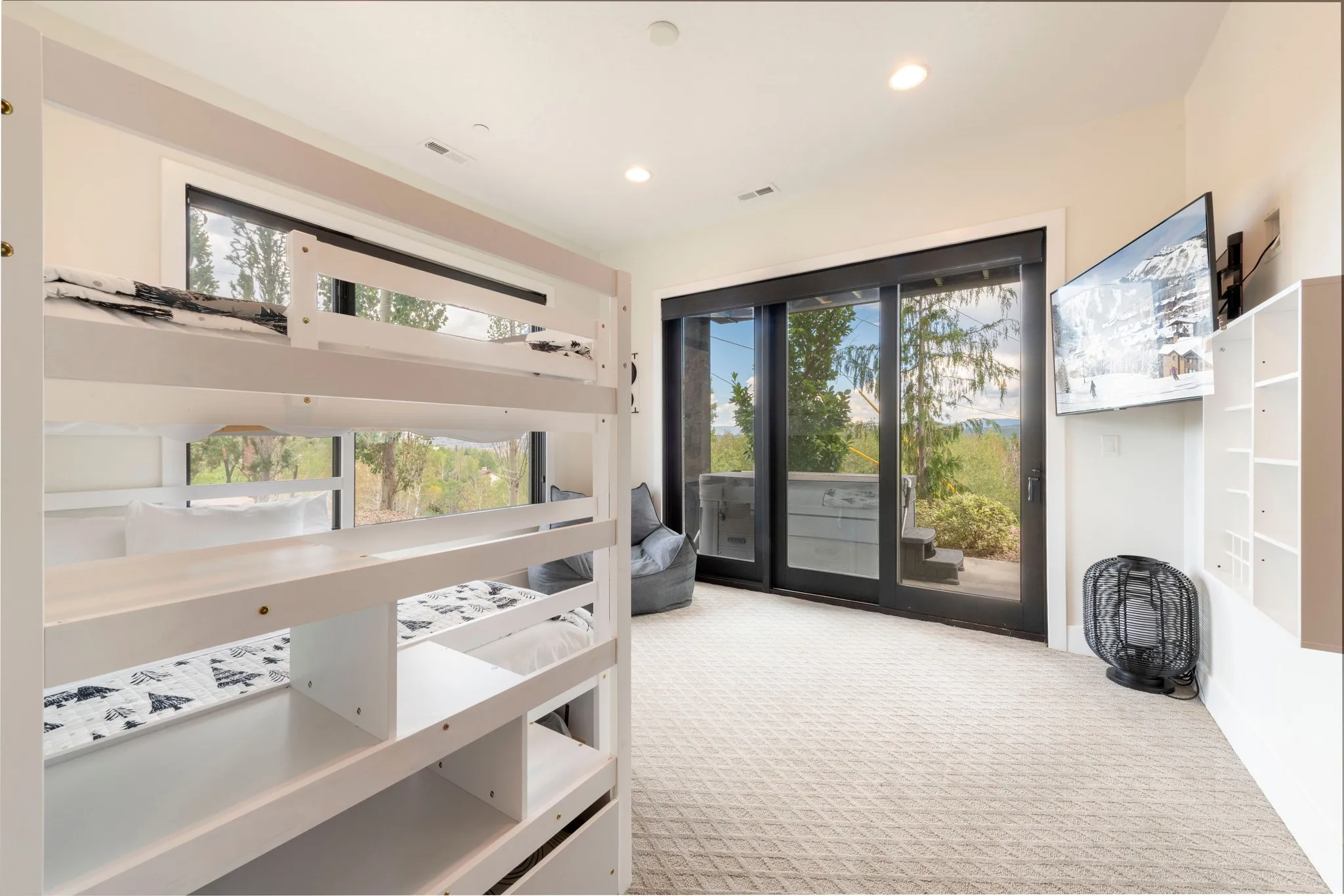 White bunk bed frame with integrated storage and steps, light-colored carpet, large sliding glass doors, built-in shelving, and recessed lighting