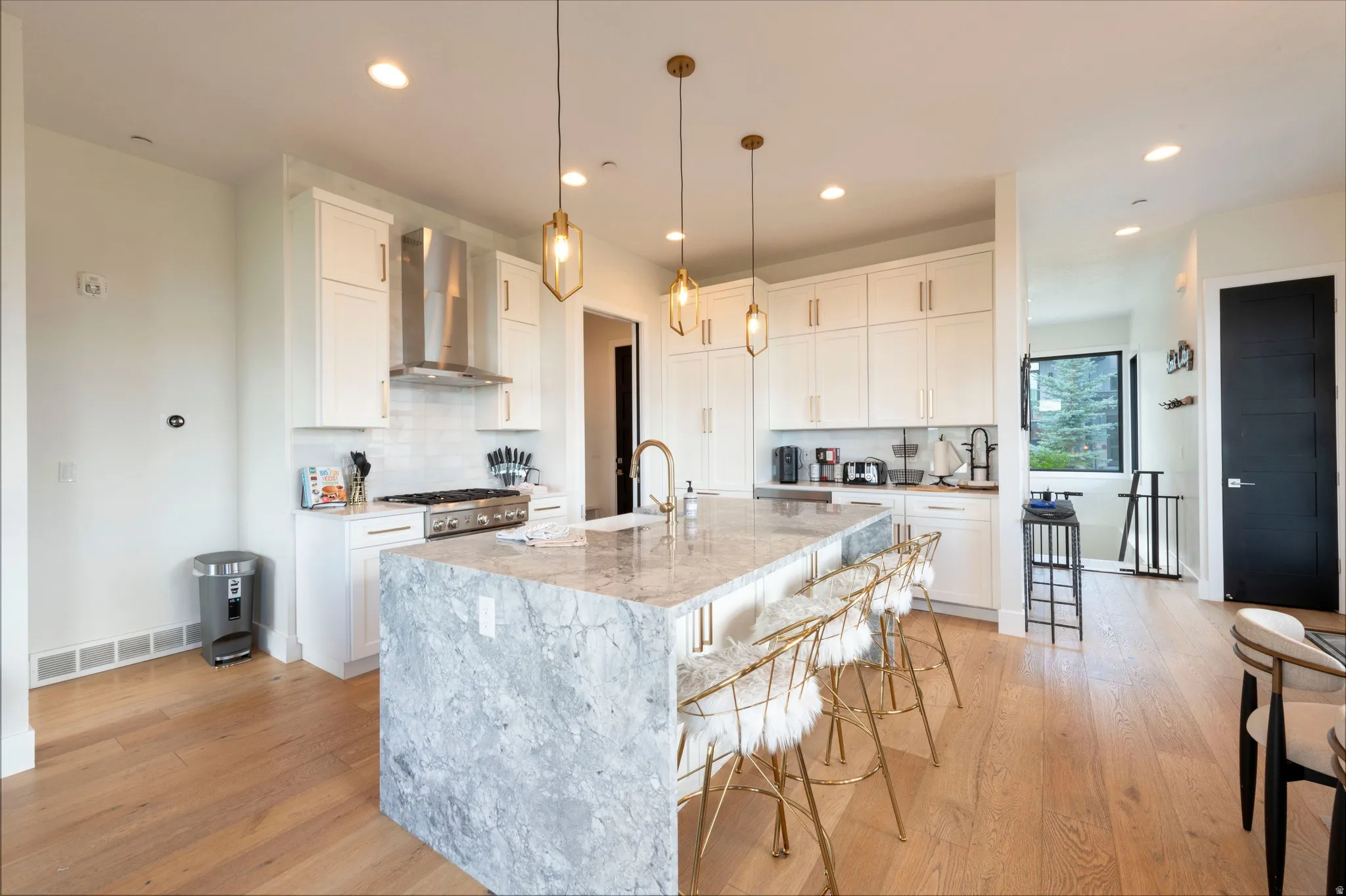 Gourmet kitchen featuring a large waterfall island with seating, stainless steel appliances, white cabinetry, and wood-finish flooring