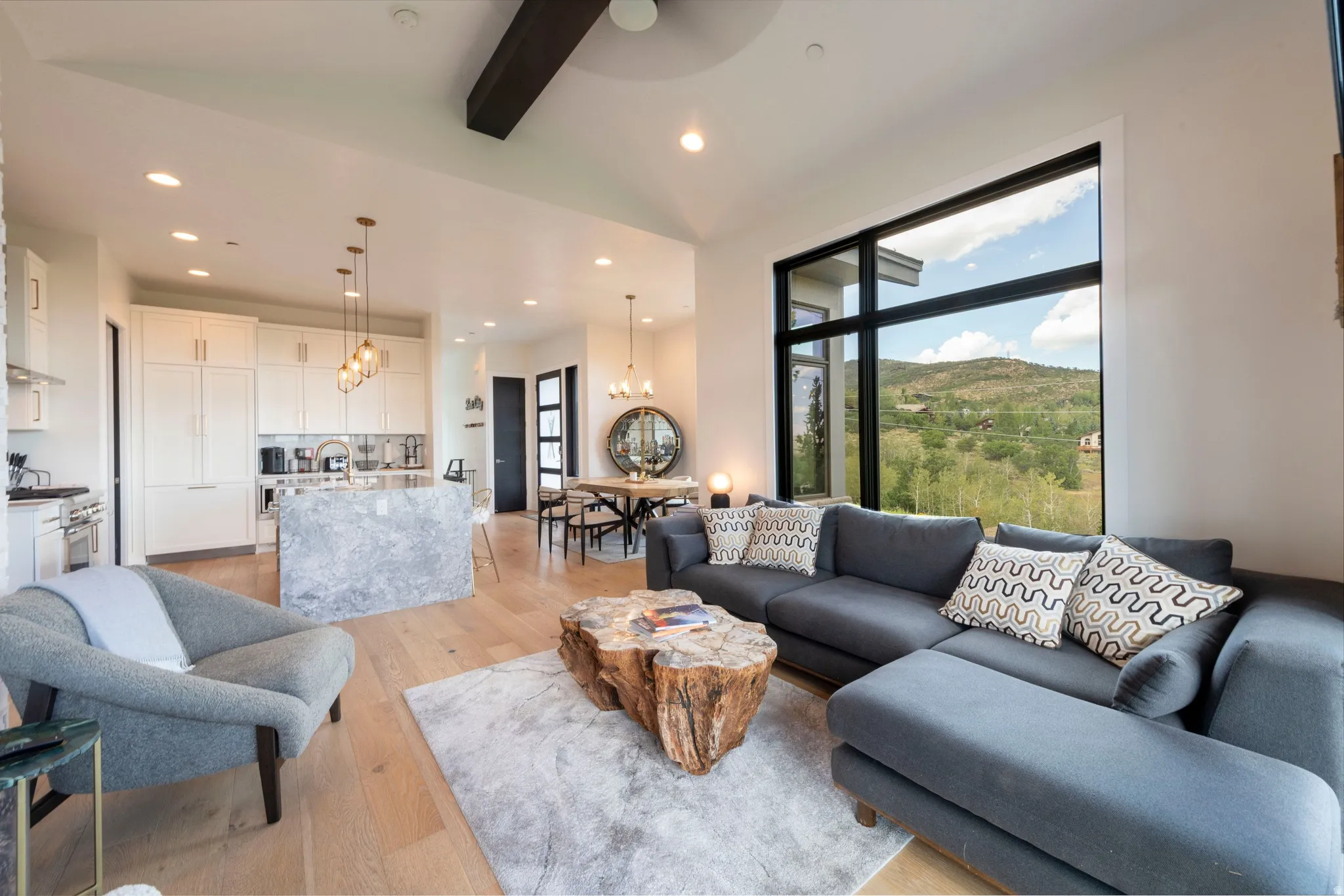 Open-concept living space featuring high ceilings, wood-finish flooring, a kitchen island with stone finish, and large windows with black frames