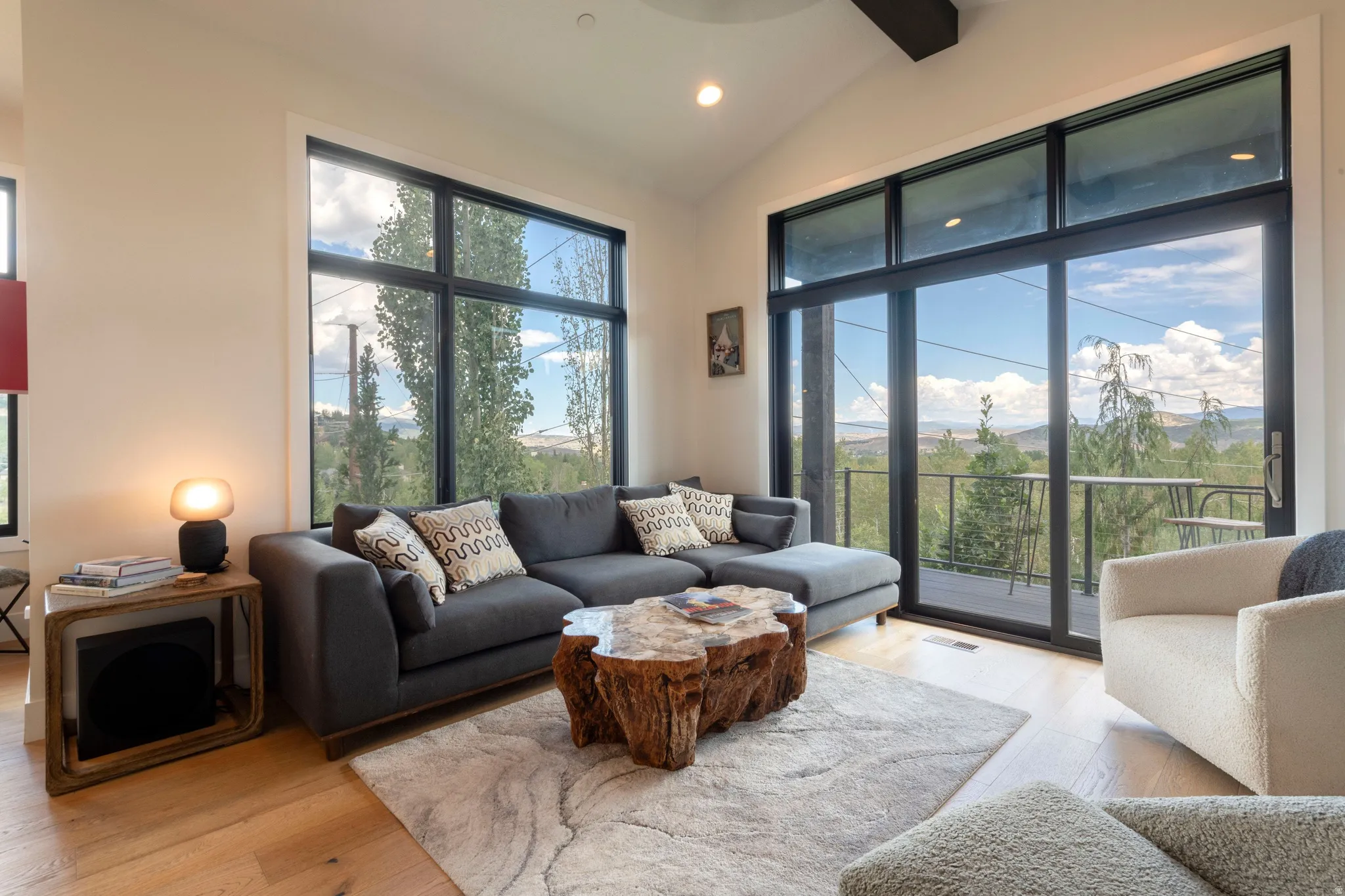 Vaulted ceiling with exposed beam, expansive window walls, and wood-finish flooring