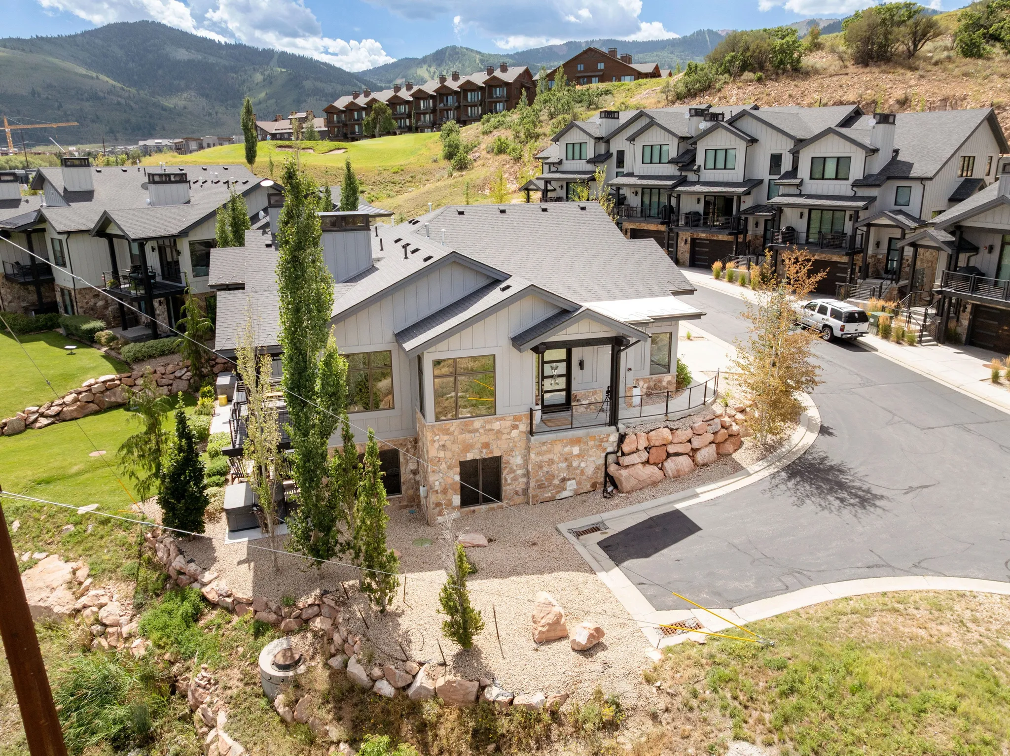 Modern property with light gray siding, natural stone accents, a dark roof, and a covered porch