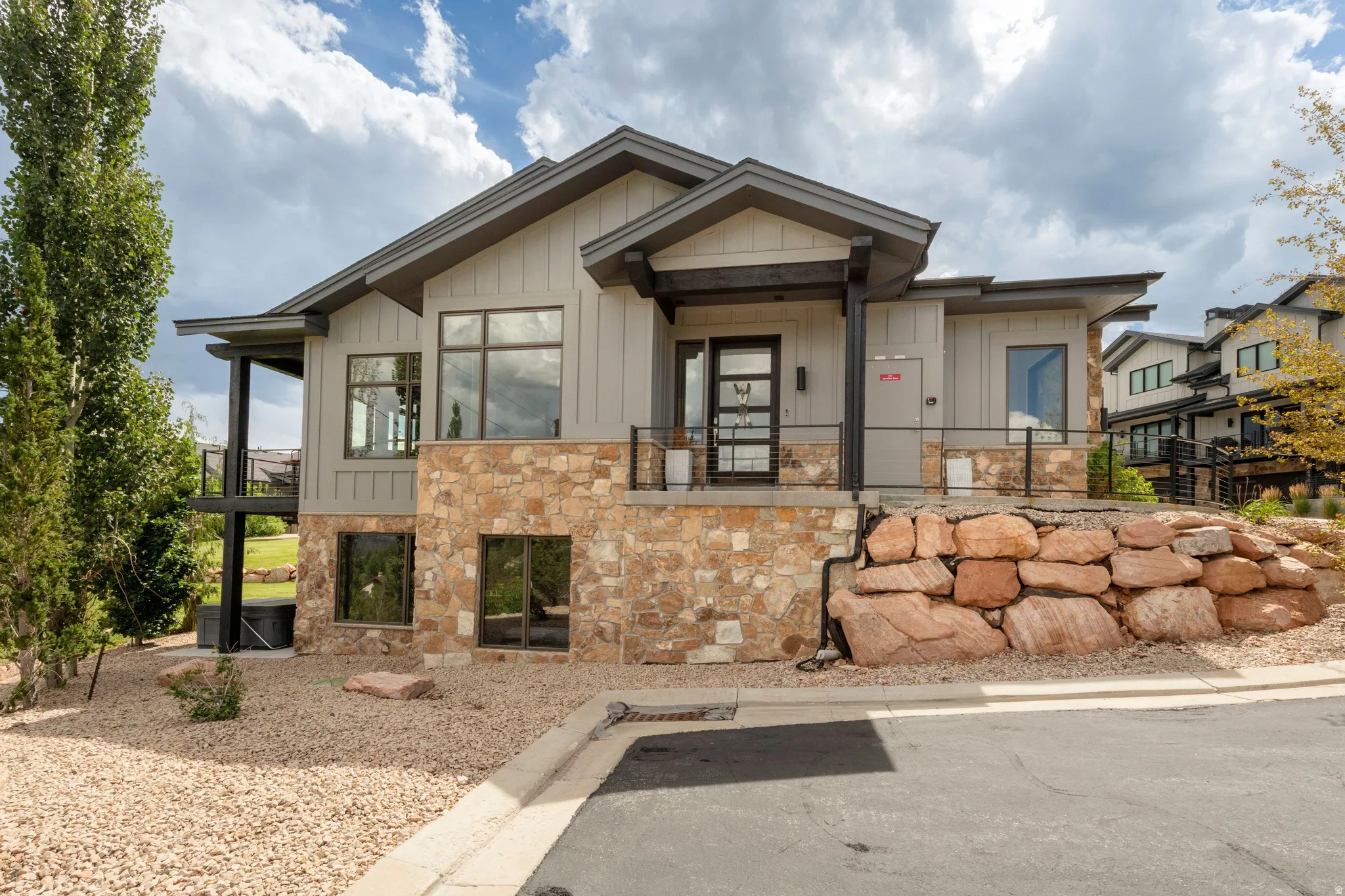 Contemporary exterior with vertical siding, stone accents, multiple large windows, a full-lite entry door, and an upper-level balcony