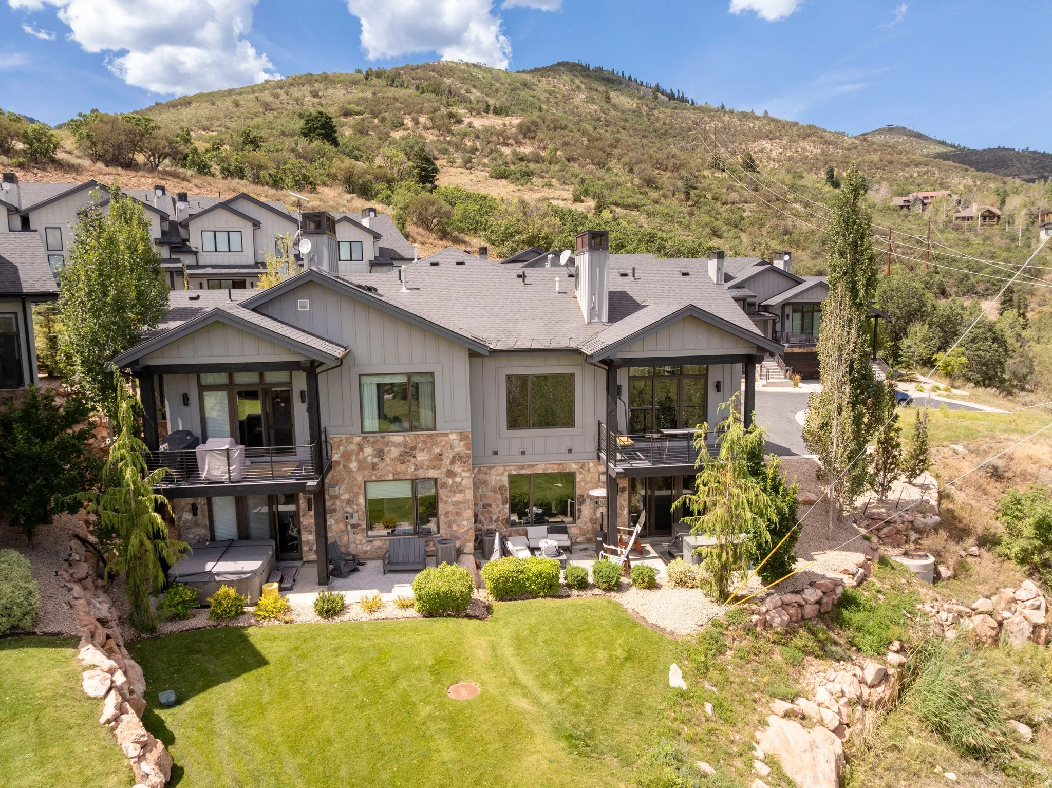 Multi-level residence featuring stone and vertical panel siding, multiple balconies, and a ground-level patio