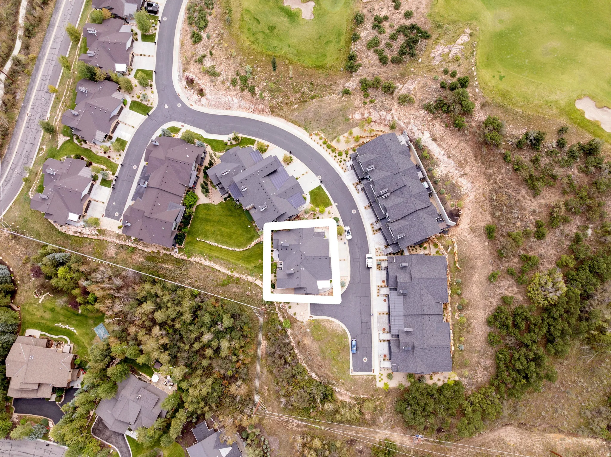 Aerial perspective of a property within a residential development, featuring a cul-de-sac and multiple structures with dark-toned roofing