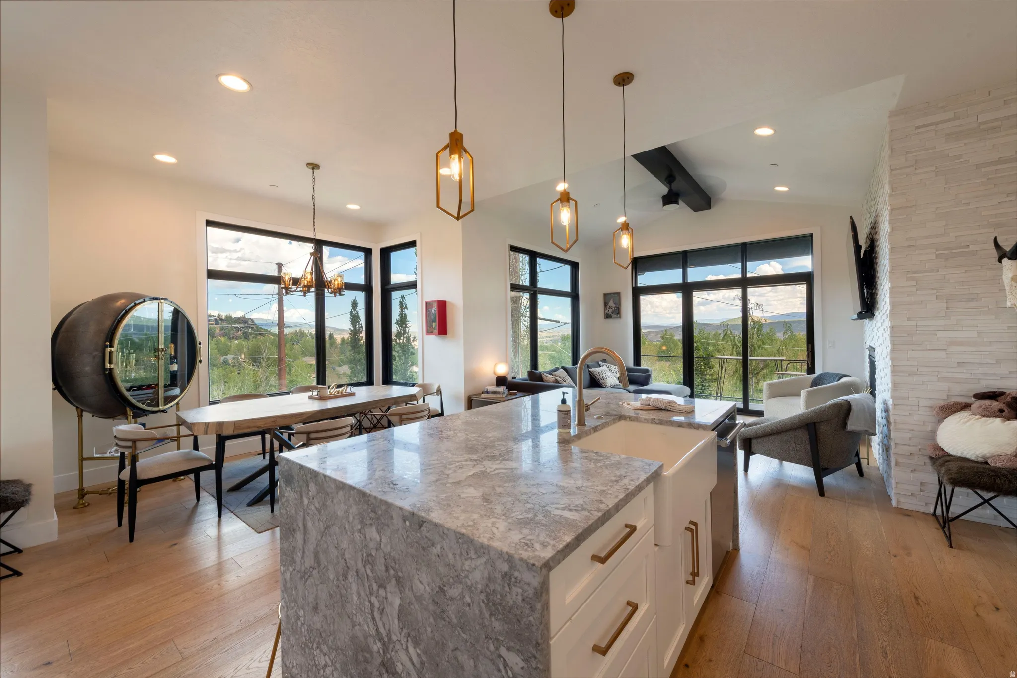 Open concept living space featuring a prominent kitchen island with a stone countertop, light wood-finish flooring, and expansive windows