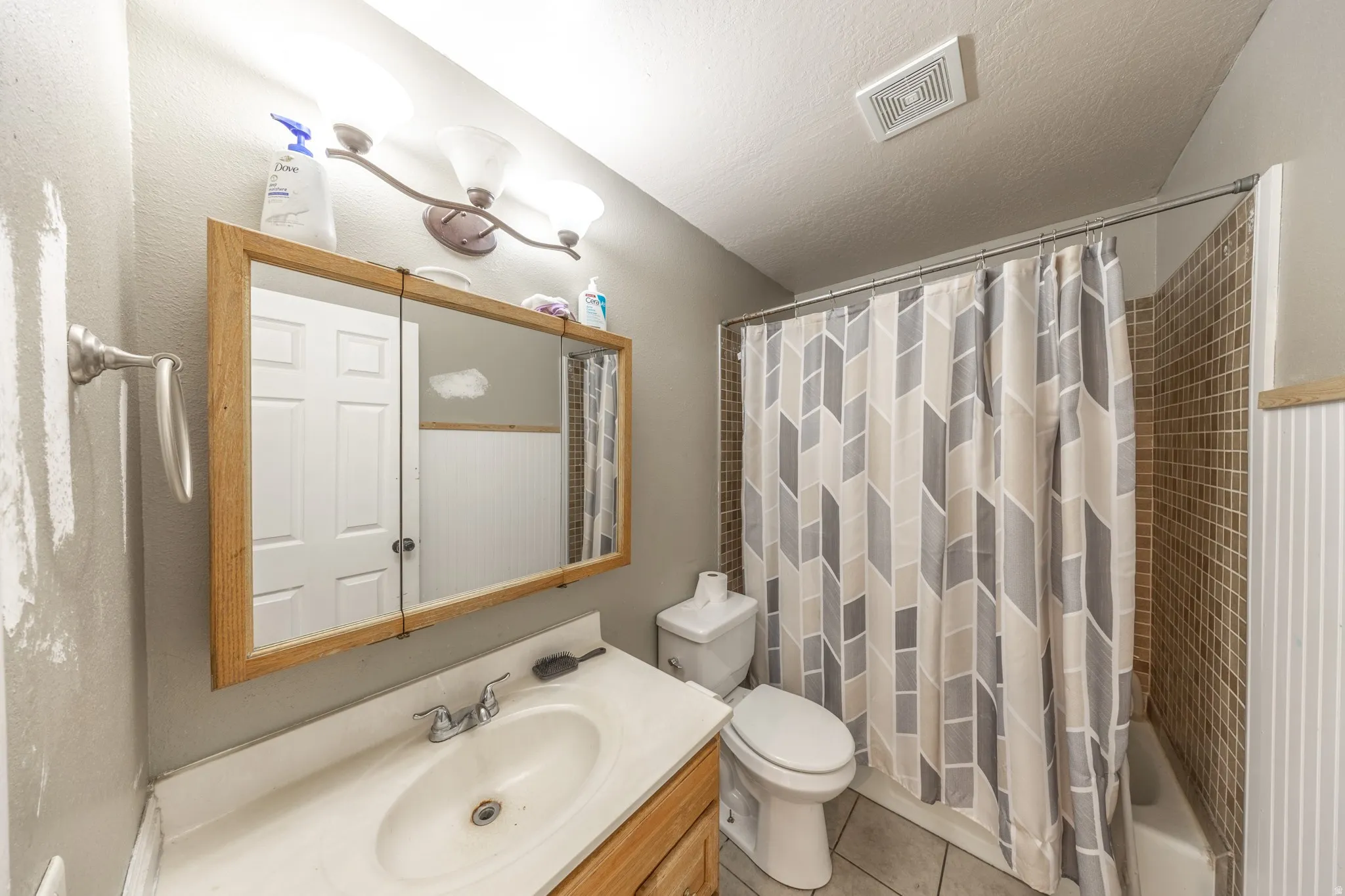 Bathroom featuring a single vanity with an integrated sink, a medicine cabinet with a wood-finish frame, a toilet, a full-size bathtub, and a tiled shower surround