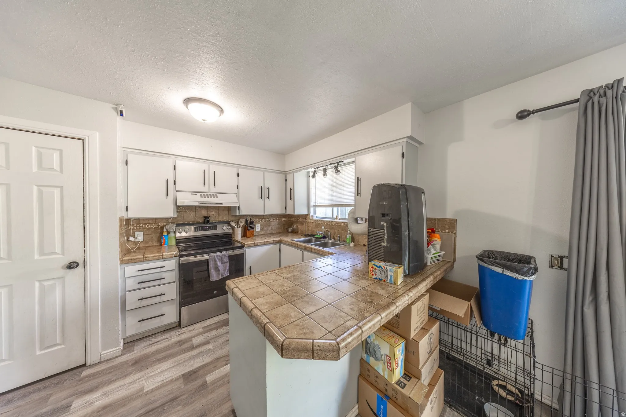 White cabinetry, tile countertops, stainless steel range, and wood-finish flooring