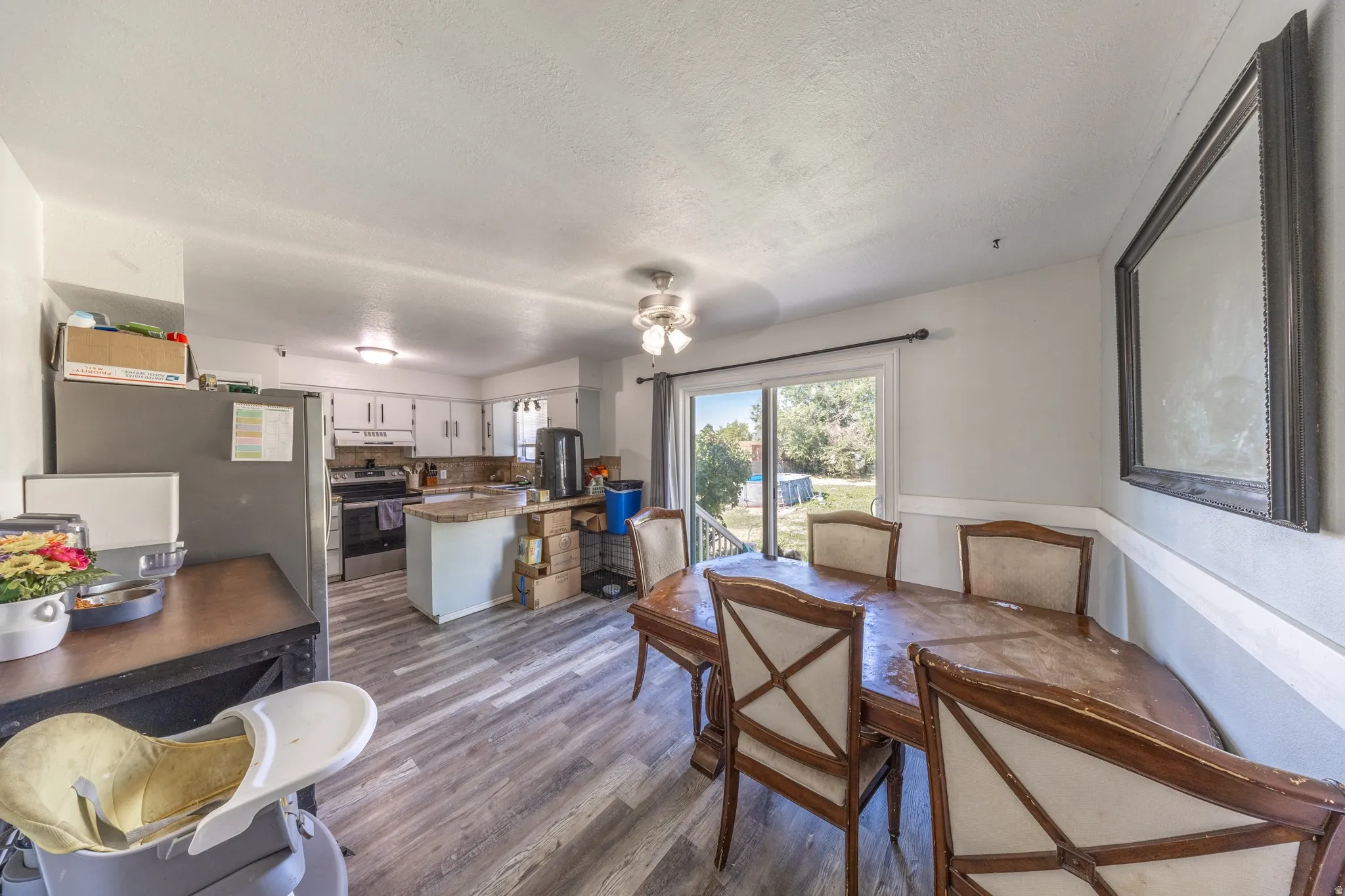 Wood-finish flooring, white cabinetry, stainless steel appliances, sliding glass door, and a ceiling fan with integrated lighting