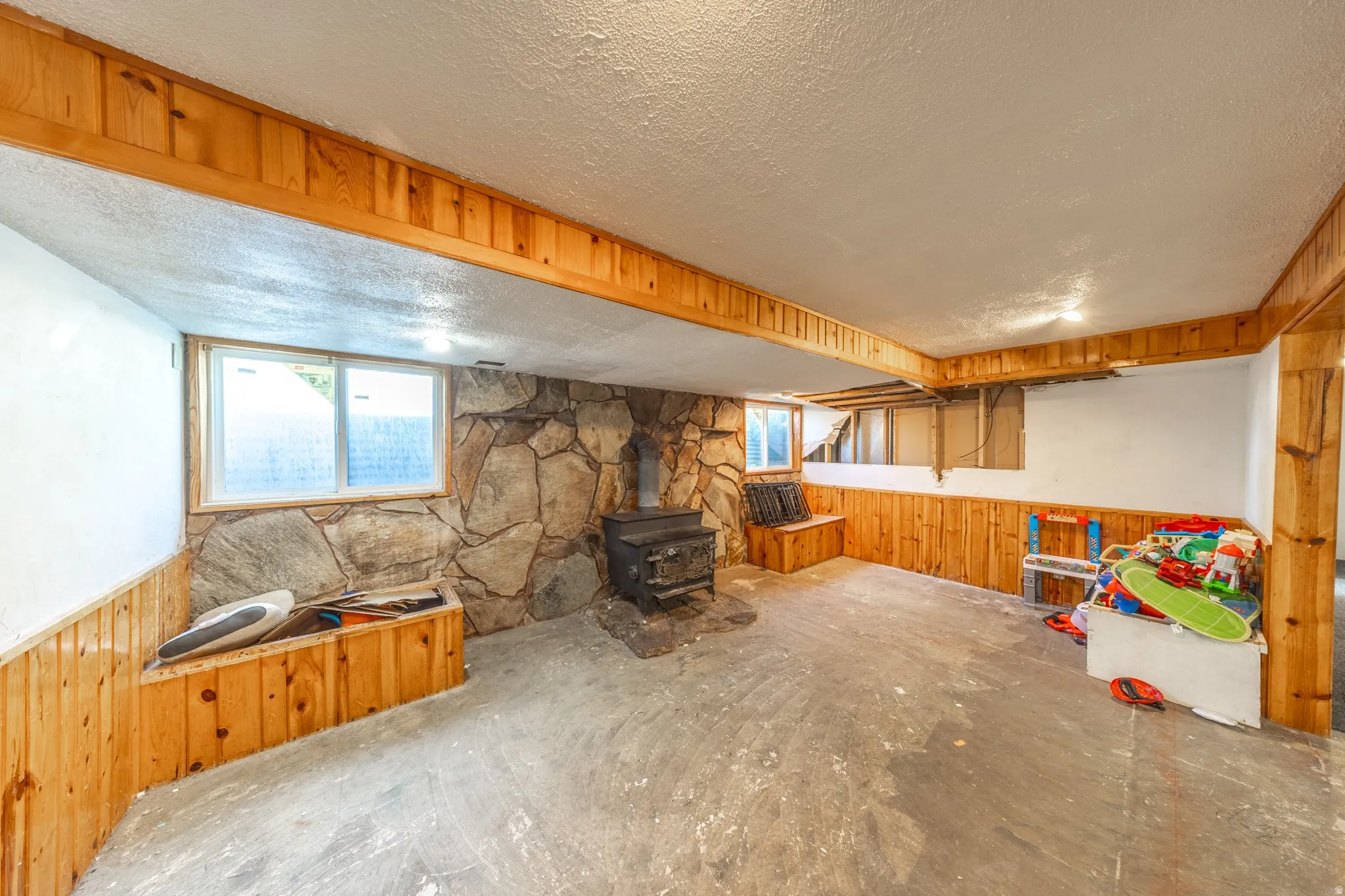 Stone-clad fireplace with a wood-burning stove, wood paneling, and built-in wood seating