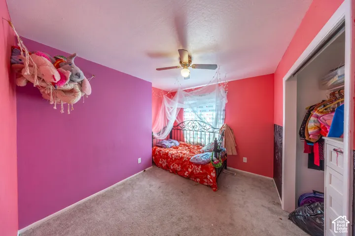 Carpeted flooring, central ceiling fan with integrated lighting, and reach-in closet